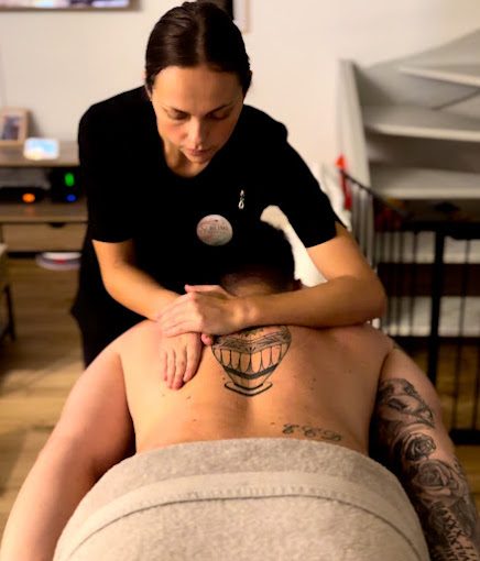 Femme massant le dos d'un client, tatouage visible sur la peau.